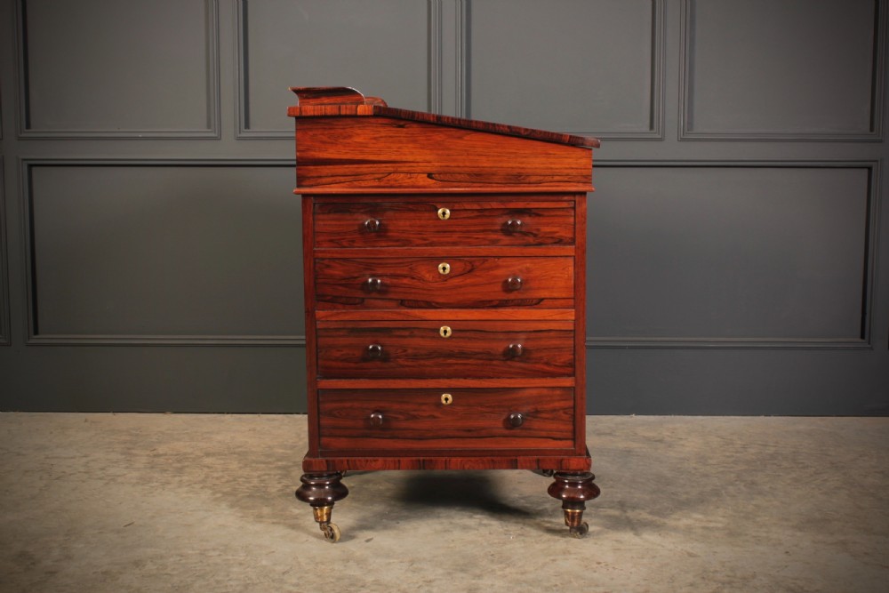 A William IV rosewood Davenport desk featuring a green leather sloped writing surface, side drawers with wooden knob handles, and turned feet on brass castors. View XVII