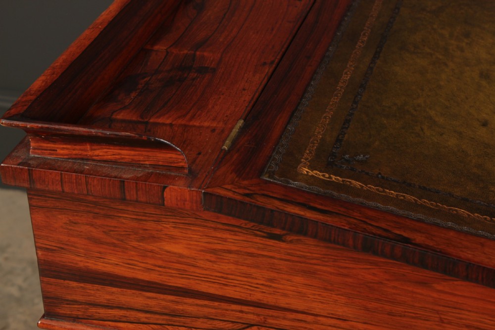 A William IV rosewood Davenport desk featuring a green leather sloped writing surface, side drawers with wooden knob handles, and turned feet on brass castors. View XVIII