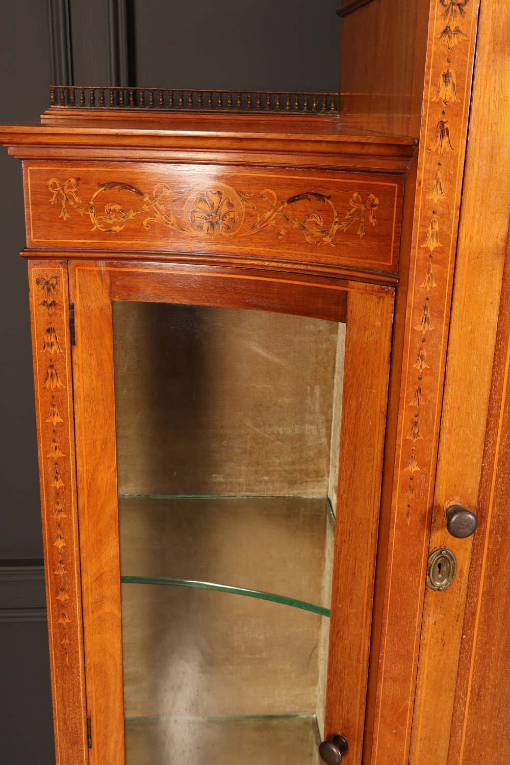 An Edwardian mahogany side cabinet with a central door featuring an urn marquetry inlay, flanked by two curved glazed display sections on tapered legs. View VII