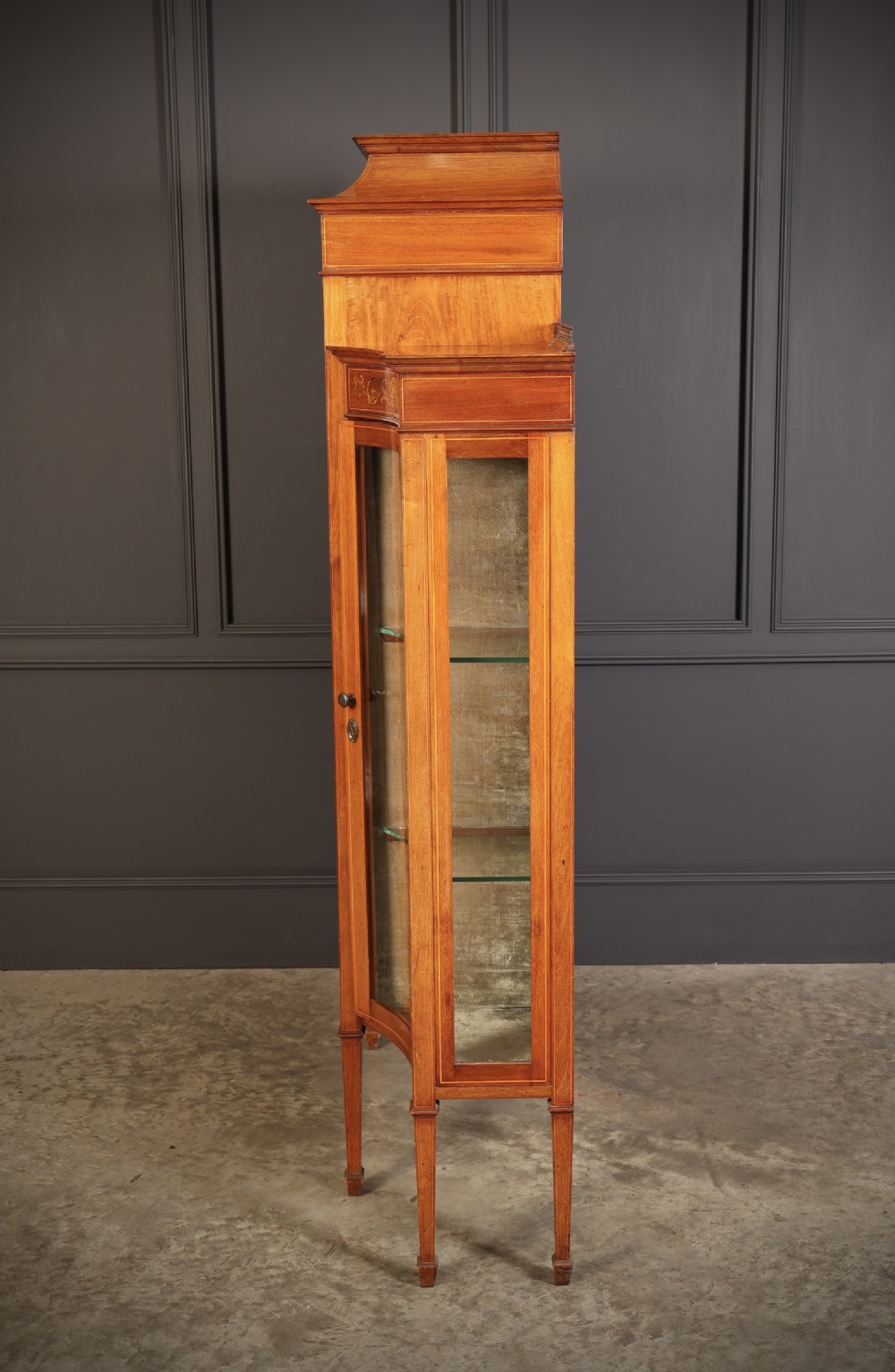 An Edwardian mahogany side cabinet with a central door featuring an urn marquetry inlay, flanked by two curved glazed display sections on tapered legs. View IX