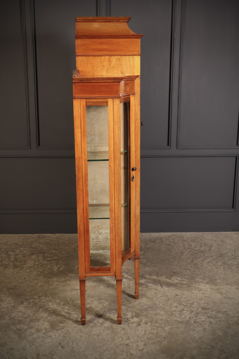 An Edwardian mahogany side cabinet with a central door featuring an urn marquetry inlay, flanked by two curved glazed display sections on tapered legs. View XI