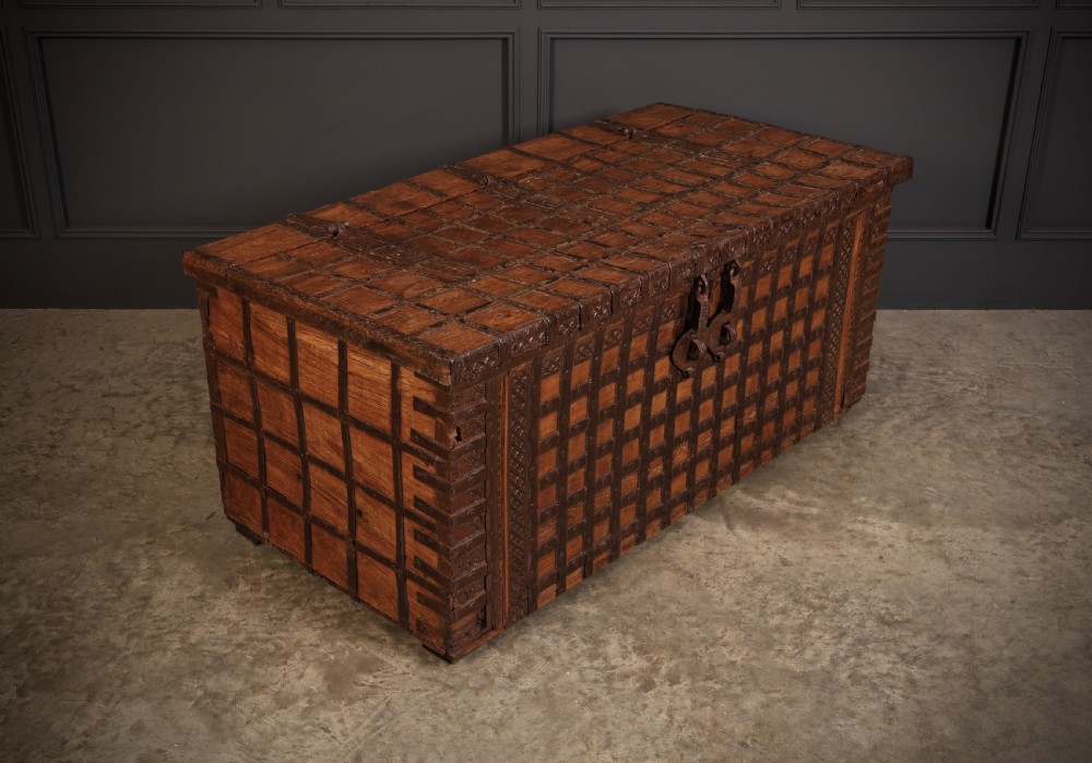 A large rectangular brown hardwood trunk reinforced with a grid of iron straps and featuring heavy iron latches on the front. View II