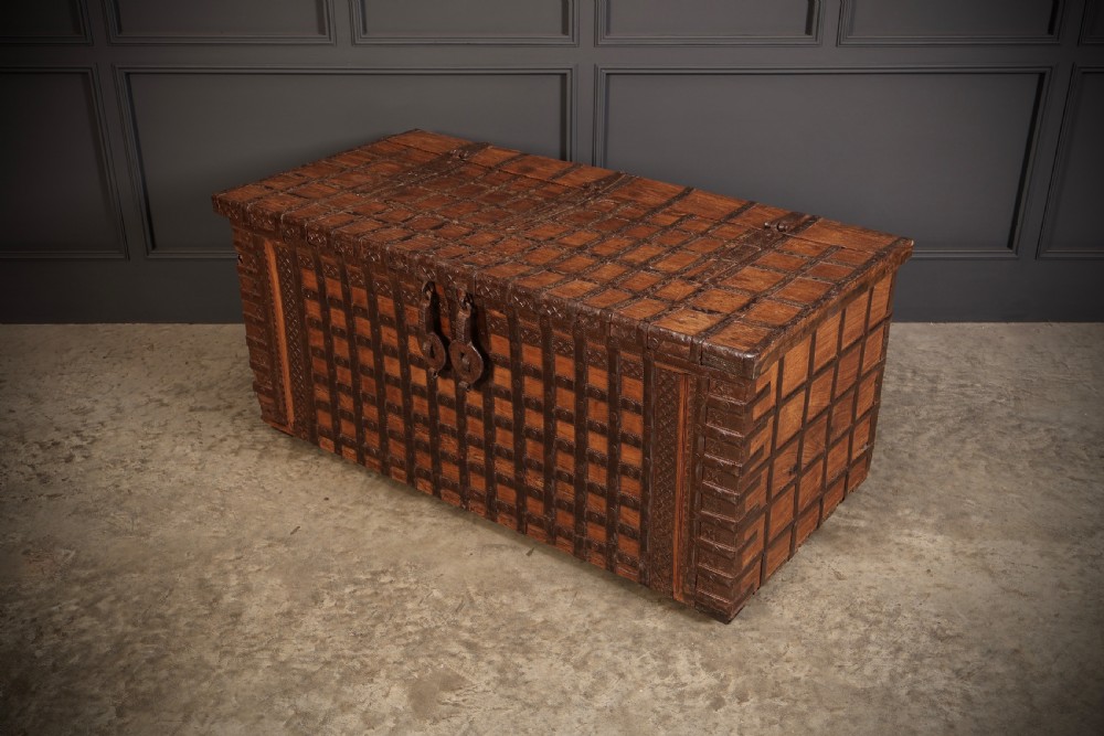 A large rectangular brown hardwood trunk reinforced with a grid of iron straps and featuring heavy iron latches on the front.