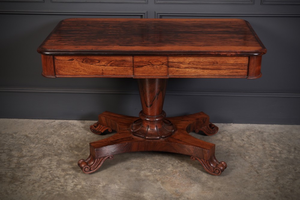 An antique rosewood library centre table featuring a rectangular figured top, two frieze drawers, a faceted pedestal column, and a quadform base with scroll feet. View II