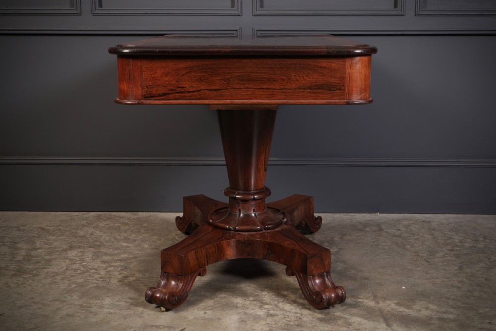 An antique rosewood library centre table featuring a rectangular figured top, two frieze drawers, a faceted pedestal column, and a quadform base with scroll feet. View III