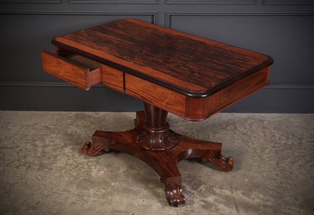 An antique rosewood library centre table featuring a rectangular figured top, two frieze drawers, a faceted pedestal column, and a quadform base with scroll feet. View V