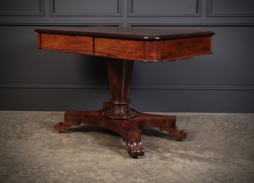 An antique rosewood library centre table featuring a rectangular figured top, two frieze drawers, a faceted pedestal column, and a quadform base with scroll feet. View VI