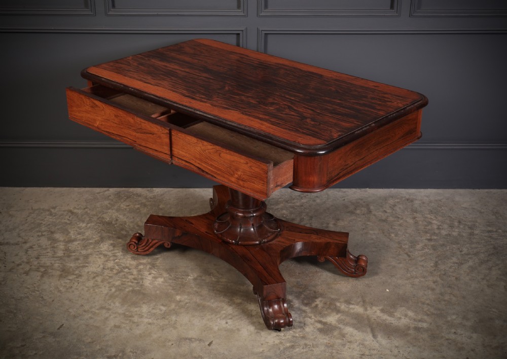 An antique rosewood library centre table featuring a rectangular figured top, two frieze drawers, a faceted pedestal column, and a quadform base with scroll feet. View VII