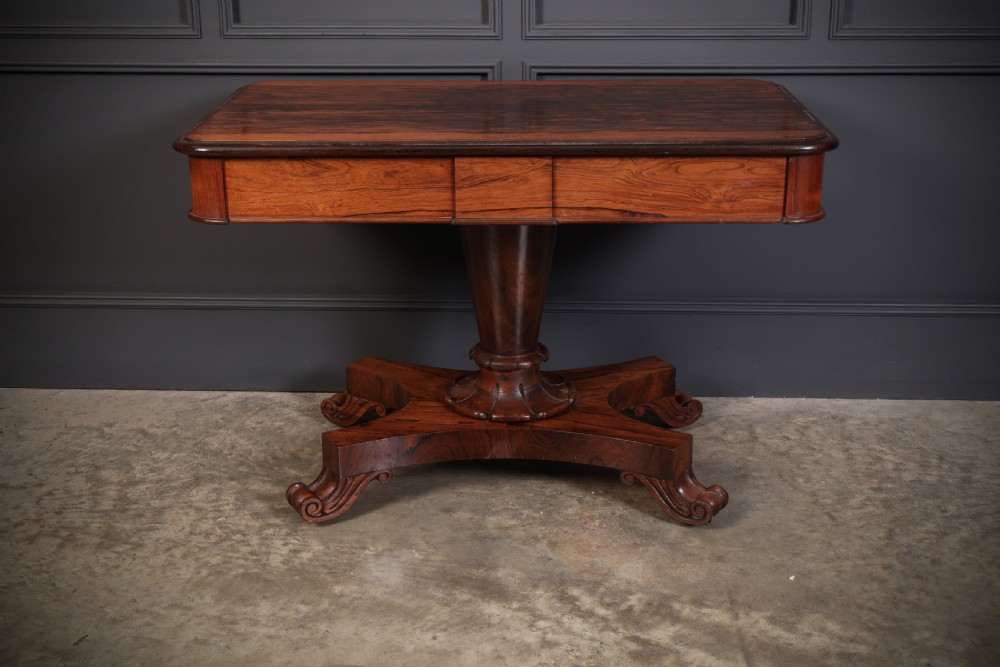 An antique rosewood library centre table featuring a rectangular figured top, two frieze drawers, a faceted pedestal column, and a quadform base with scroll feet. View IX