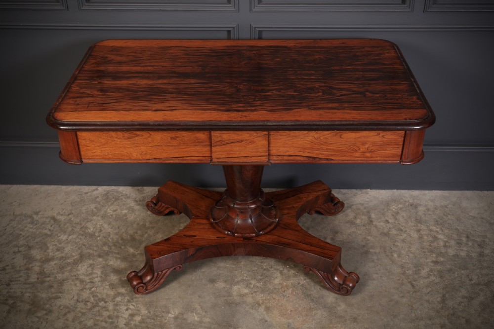 An antique rosewood library centre table featuring a rectangular figured top, two frieze drawers, a faceted pedestal column, and a quadform base with scroll feet. View X