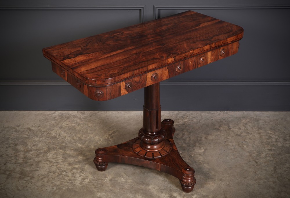An antique Regency rosewood card table featuring a hinged rectangular top, rosette-decorated frieze, turned column, and triform pedestal base. View V