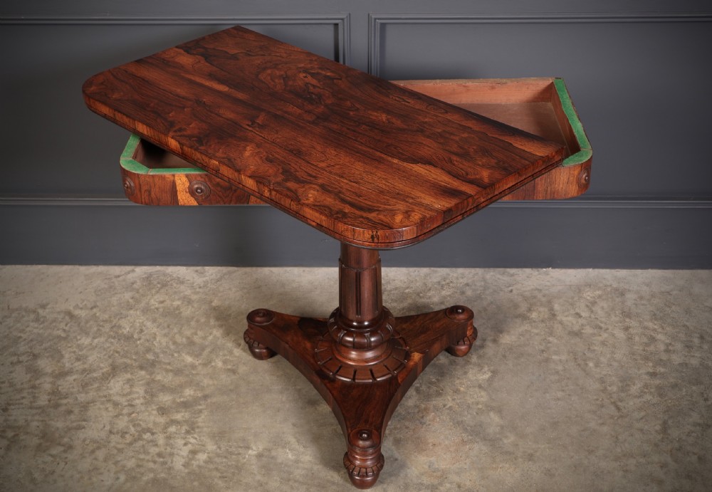 An antique Regency rosewood card table featuring a hinged rectangular top, rosette-decorated frieze, turned column, and triform pedestal base. View VIII