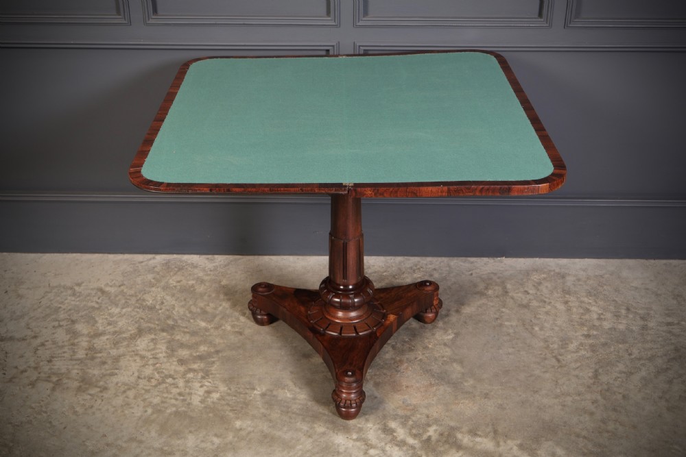 An antique Regency rosewood card table featuring a hinged rectangular top, rosette-decorated frieze, turned column, and triform pedestal base. View IX