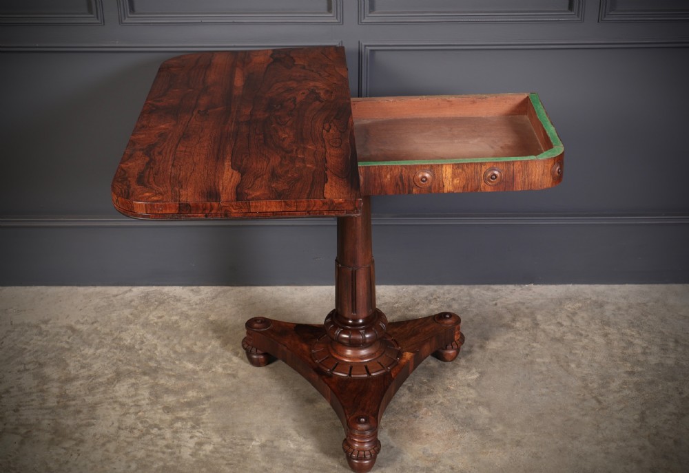 An antique Regency rosewood card table featuring a hinged rectangular top, rosette-decorated frieze, turned column, and triform pedestal base. View X