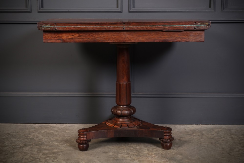 An antique Regency rosewood card table featuring a hinged rectangular top, rosette-decorated frieze, turned column, and triform pedestal base. View XII