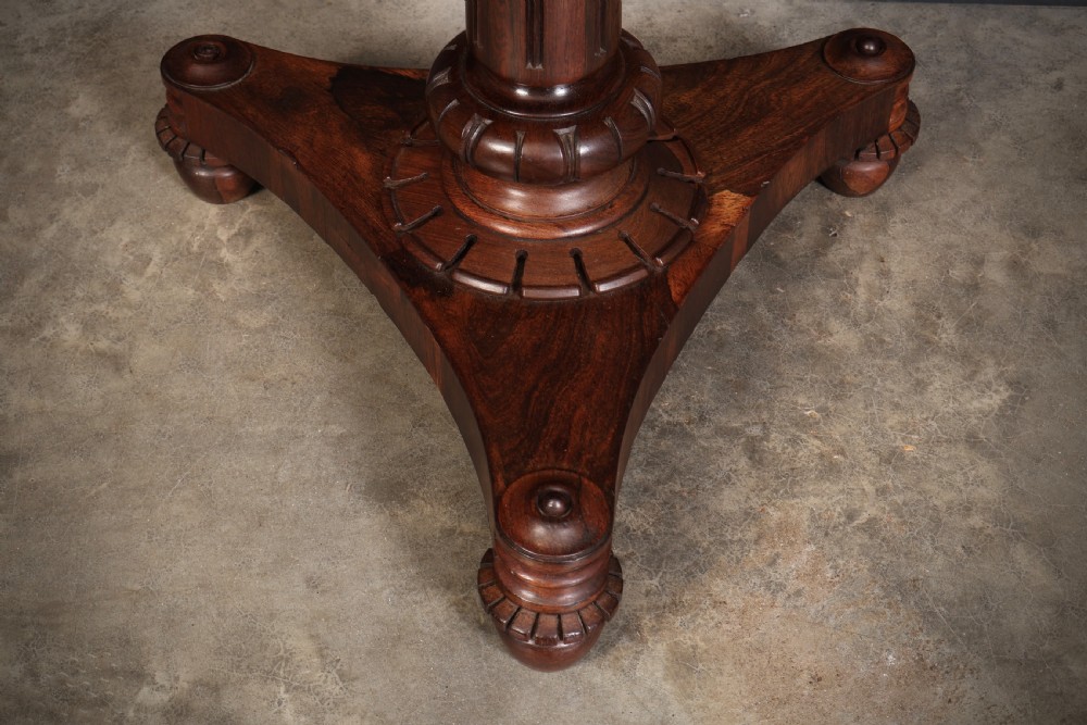 An antique Regency rosewood card table featuring a hinged rectangular top, rosette-decorated frieze, turned column, and triform pedestal base. View XIV