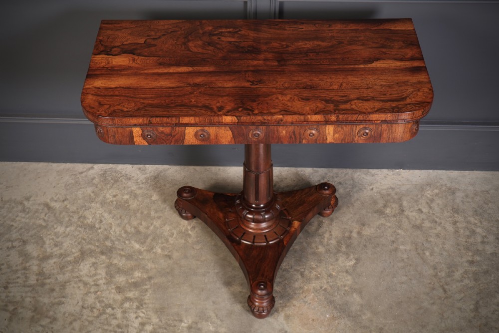 An antique Regency rosewood card table featuring a hinged rectangular top, rosette-decorated frieze, turned column, and triform pedestal base. View XV