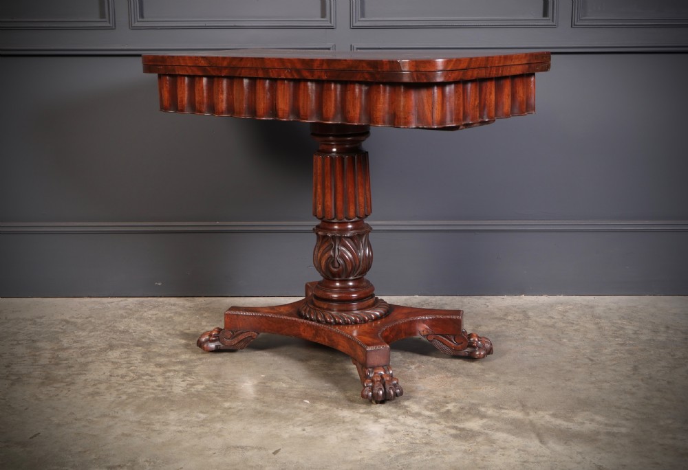 A Regency mahogany card table featuring a fold-over rectangular top, reeded apron, carved central pedestal, and quadripartite base with paw feet. View VI