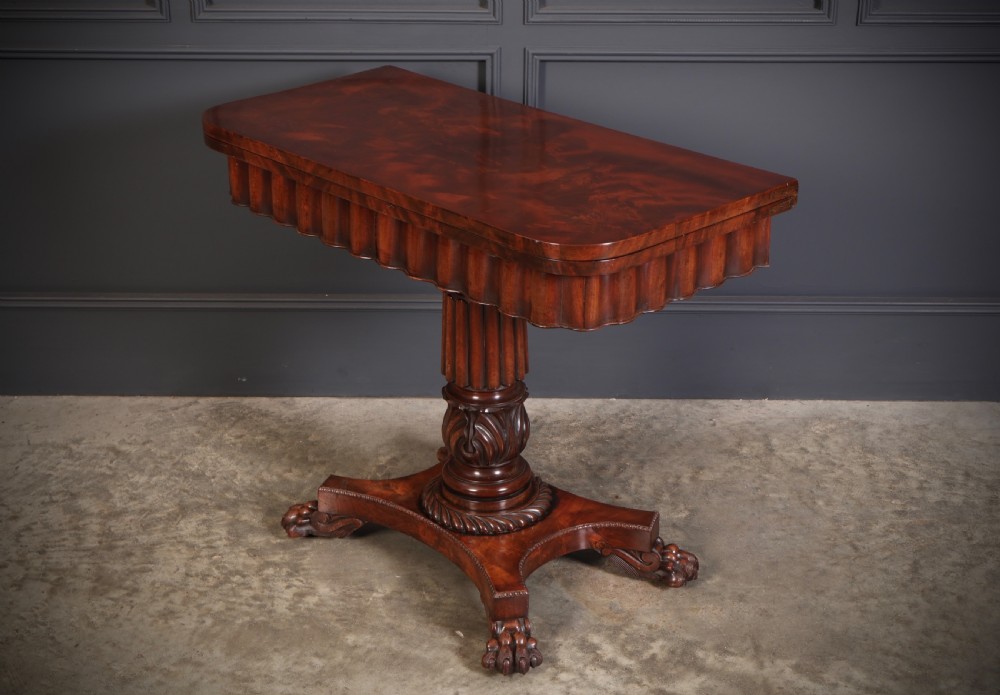 A Regency mahogany card table featuring a fold-over rectangular top, reeded apron, carved central pedestal, and quadripartite base with paw feet.