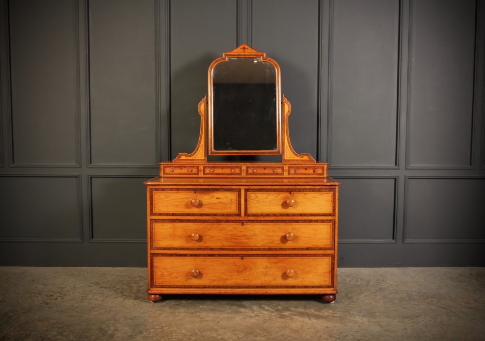 A Victorian pine dressing chest featuring dark stencilled border detailing, turned wooden handles, two short over two long drawers, small jewellery drawers, and an arched swivel mirror.