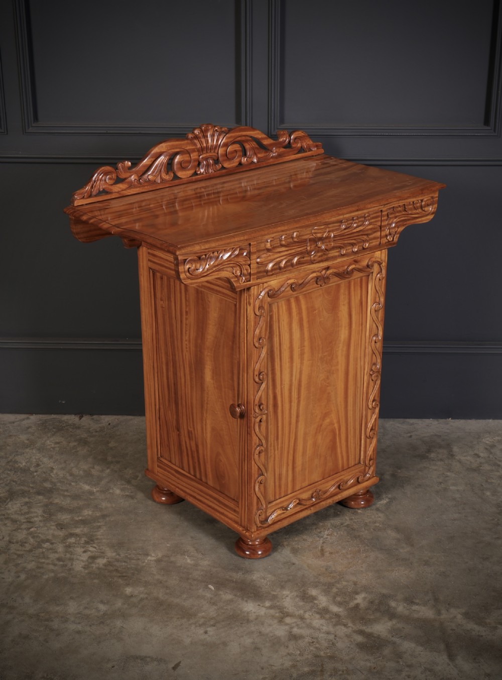 A carved satinwood Anglo-Indian side cabinet featuring a scroll-carved gallery back, panelled door, and turned feet. View VIII