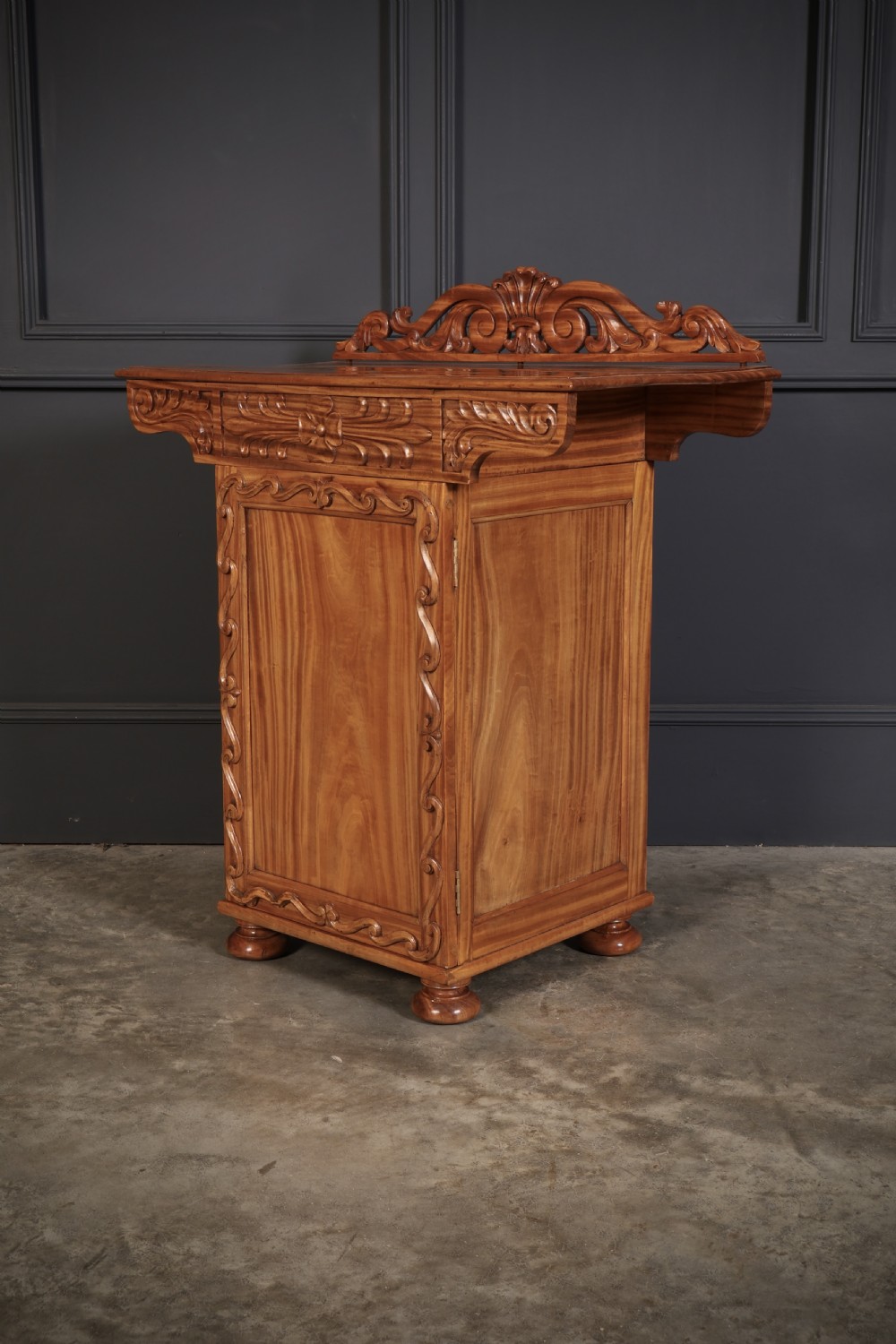 A carved satinwood Anglo-Indian side cabinet featuring a scroll-carved gallery back, panelled door, and turned feet.