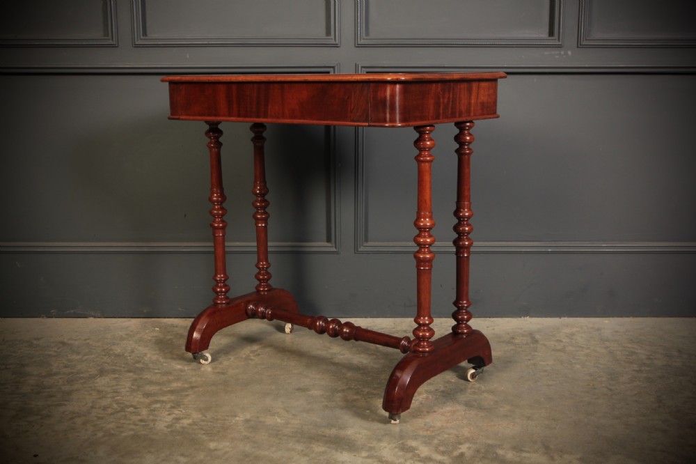 An early Victorian polished mahogany side table featuring turned dual pedestal legs, a central turned stretcher, and curved feet on castors. View III