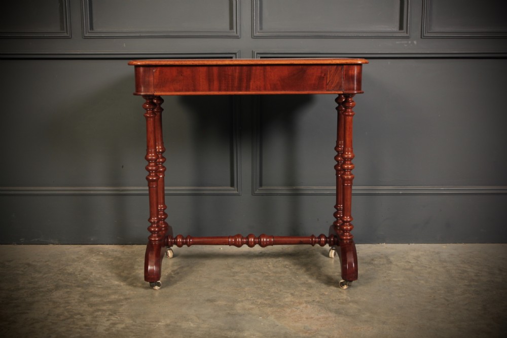An early Victorian polished mahogany side table featuring turned dual pedestal legs, a central turned stretcher, and curved feet on castors. View V