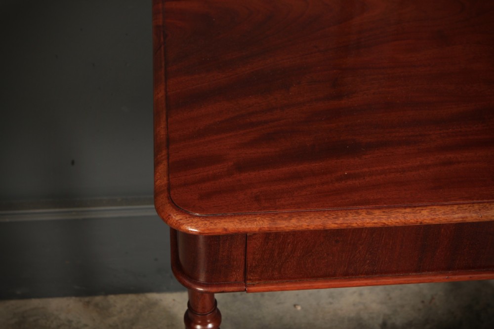 An early Victorian polished mahogany side table featuring turned dual pedestal legs, a central turned stretcher, and curved feet on castors. View VII
