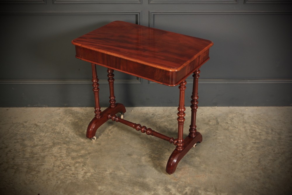 An early Victorian polished mahogany side table featuring turned dual pedestal legs, a central turned stretcher, and curved feet on castors. View IX