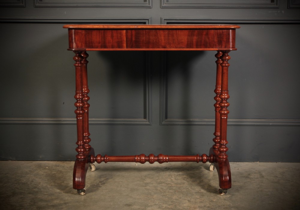 An early Victorian polished mahogany side table featuring turned dual pedestal legs, a central turned stretcher, and curved feet on castors. View X