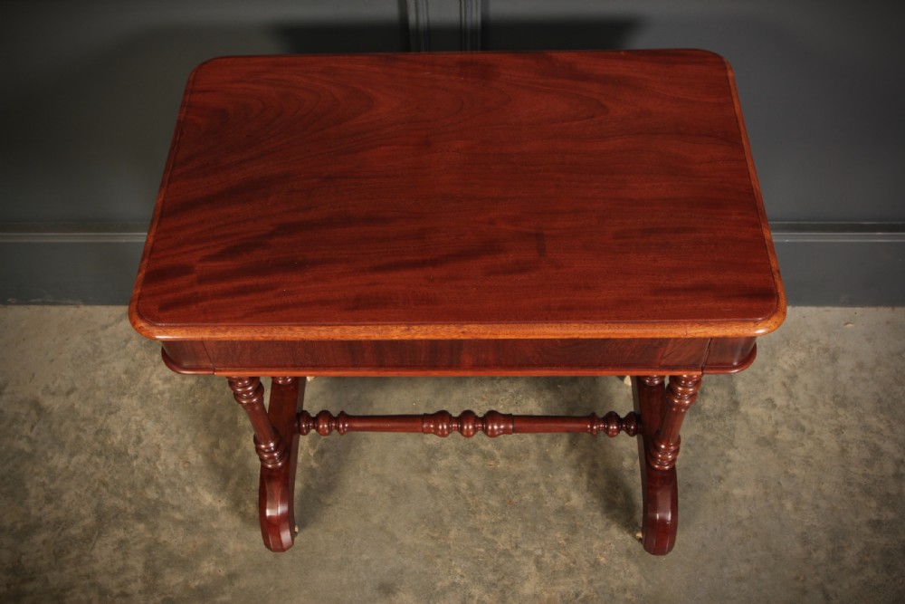 An early Victorian polished mahogany side table featuring turned dual pedestal legs, a central turned stretcher, and curved feet on castors. View XI