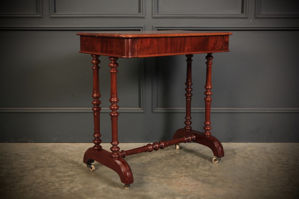 An early Victorian polished mahogany side table featuring turned dual pedestal legs, a central turned stretcher, and curved feet on castors. View XII