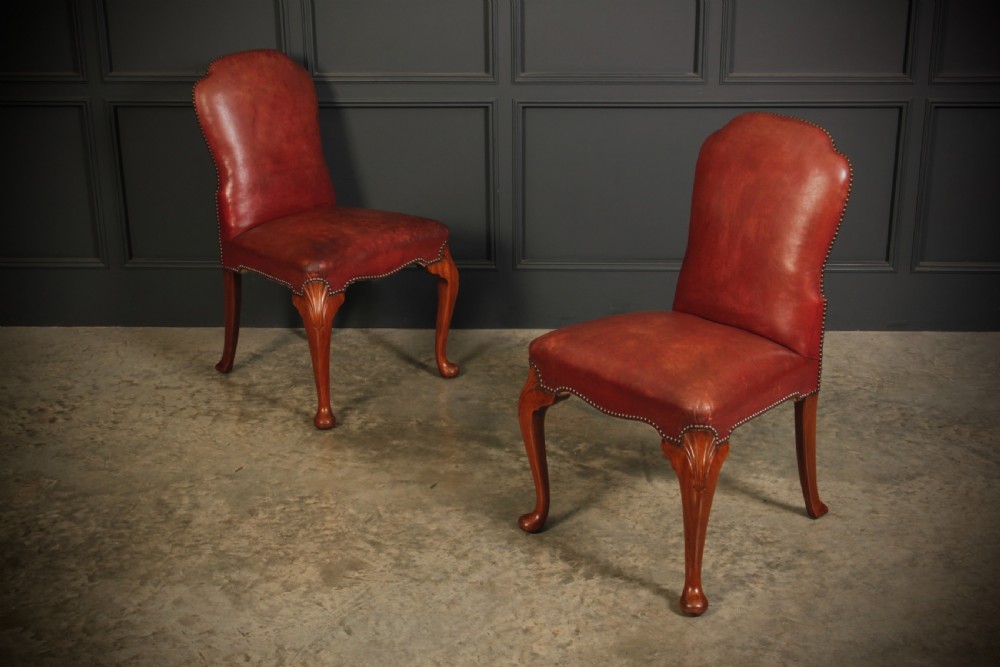 A pair of Queen Anne style side chairs upholstered in deep red leather with brass stud trimming and carved walnut cabriole legs.