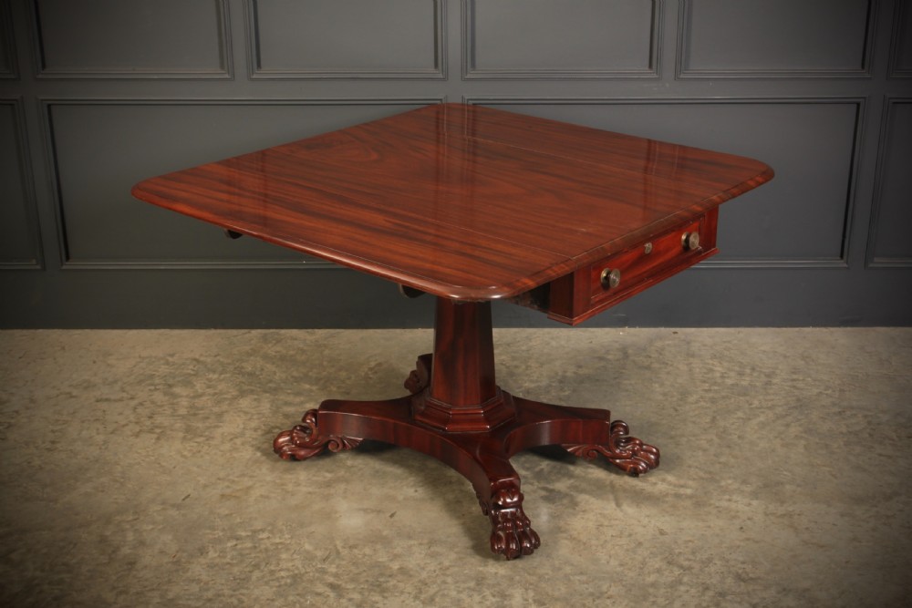 A William IV dark mahogany Pembroke table featuring two drop-down leaves, a single drawer with turned wooden knobs, a central pedestal, and a four-pointed base ending in carved claw feet.