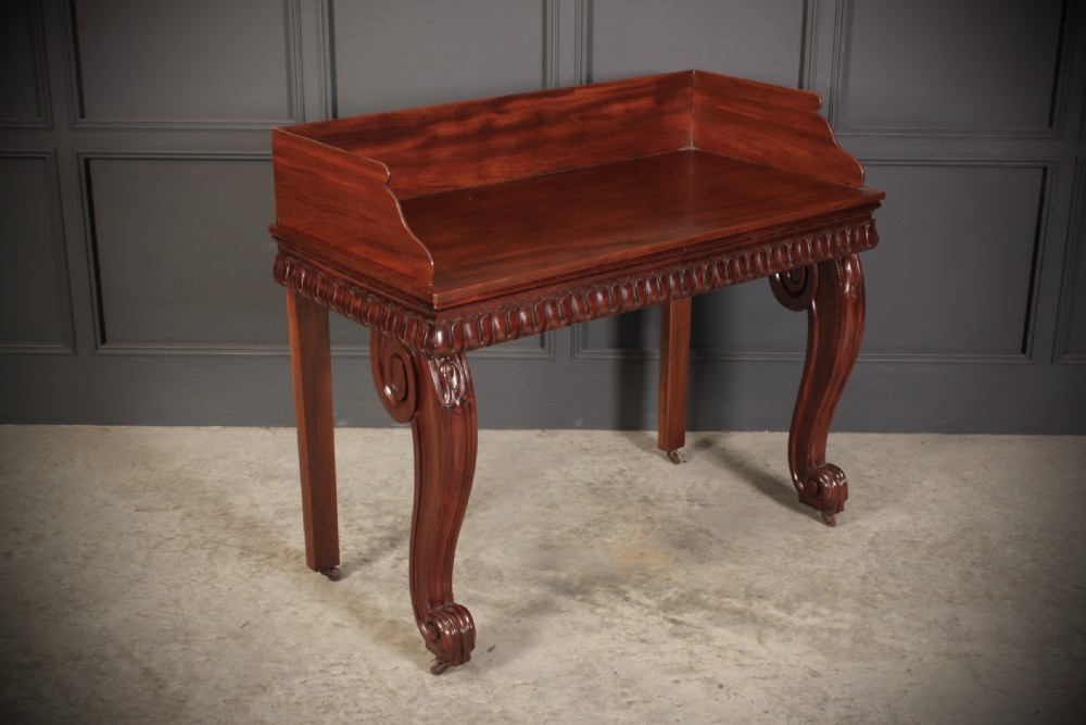 A William IV mahogany console table featuring a raised gallery back, gadrooned edge detailing, and bold S-scroll front legs on brass castors.