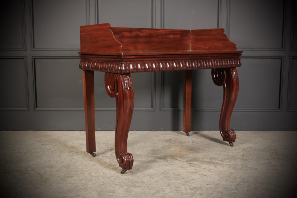 A William IV mahogany console table featuring a raised gallery back, gadrooned edge detailing, and bold S-scroll front legs on brass castors. View VII