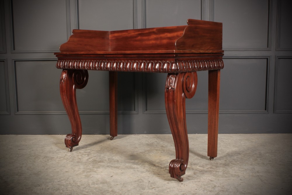 A William IV mahogany console table featuring a raised gallery back, gadrooned edge detailing, and bold S-scroll front legs on brass castors. View IX