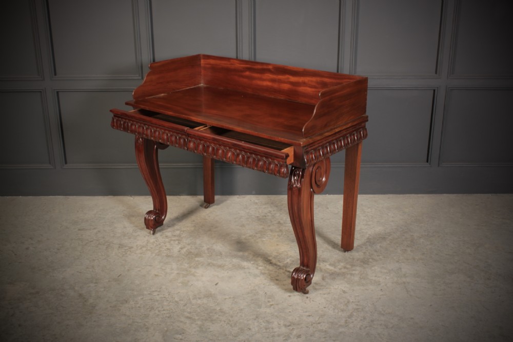 A William IV mahogany console table featuring a raised gallery back, gadrooned edge detailing, and bold S-scroll front legs on brass castors. View X