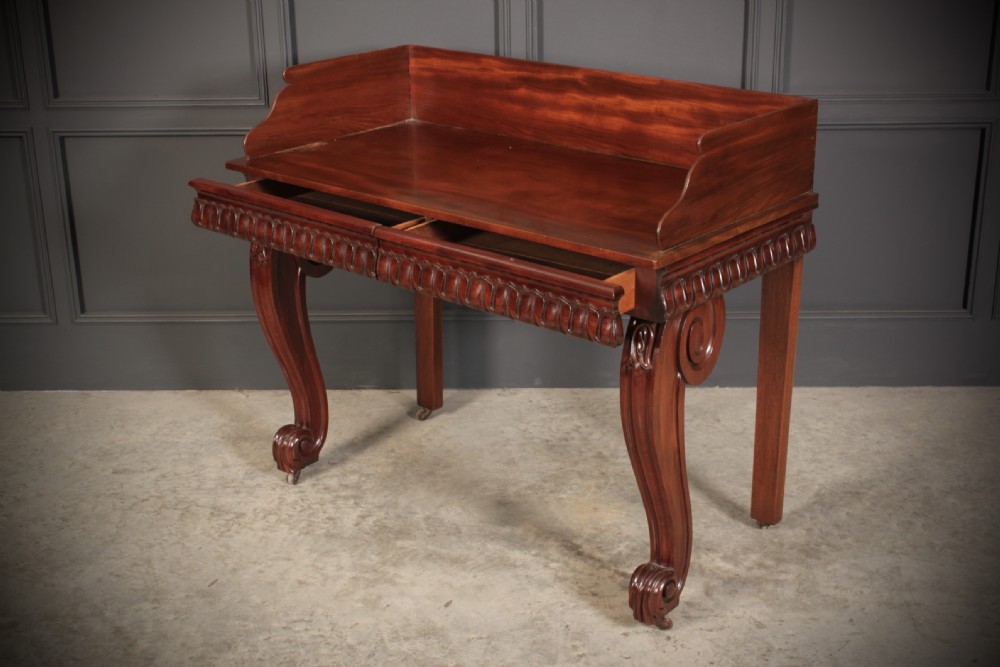 A William IV mahogany console table featuring a raised gallery back, gadrooned edge detailing, and bold S-scroll front legs on brass castors. View XI