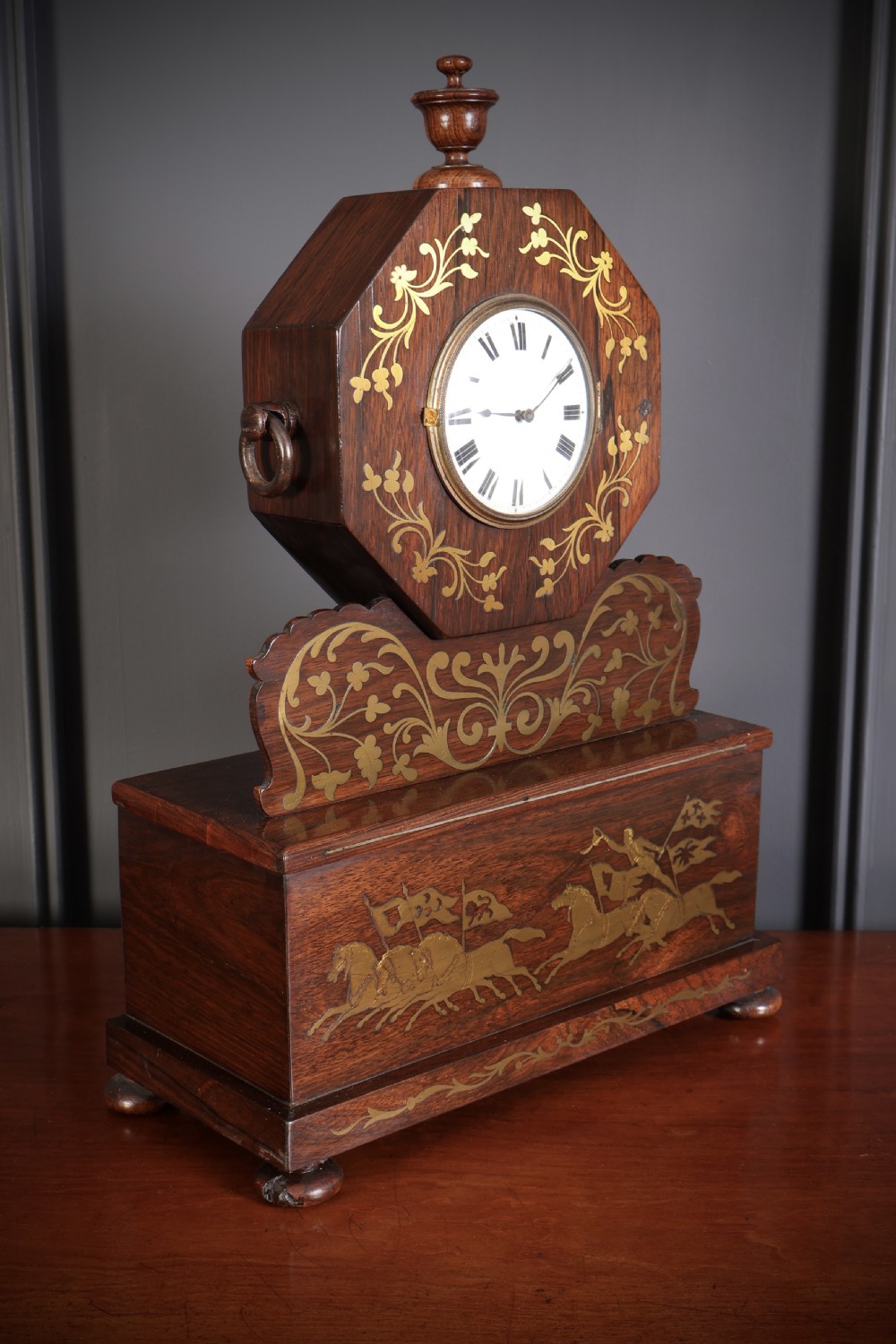 A Regency dark rosewood mantel clock with intricate brass inlay, an octagonal dial surround, and an equestrian brass scene on the base plinth. View III