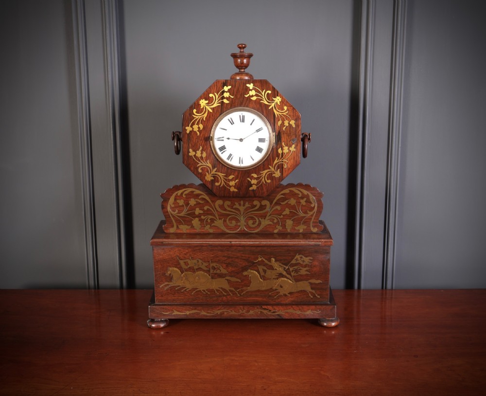 A Regency dark rosewood mantel clock with intricate brass inlay, an octagonal dial surround, and an equestrian brass scene on the base plinth. View V