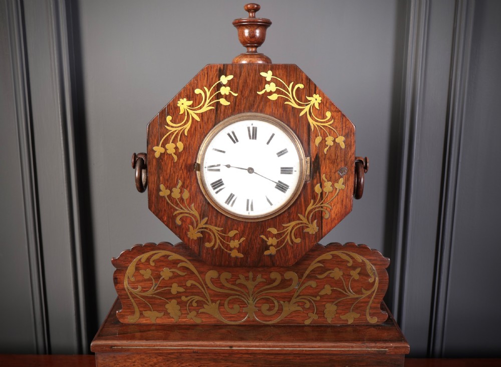 A Regency dark rosewood mantel clock with intricate brass inlay, an octagonal dial surround, and an equestrian brass scene on the base plinth. View XI