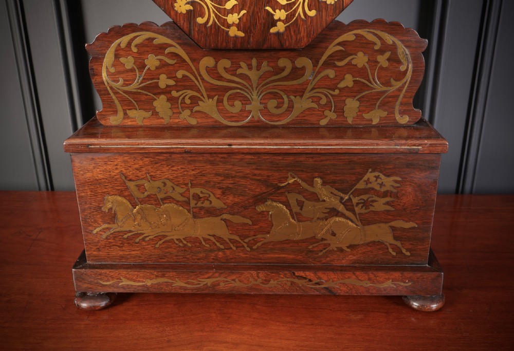 A Regency dark rosewood mantel clock with intricate brass inlay, an octagonal dial surround, and an equestrian brass scene on the base plinth. View XII