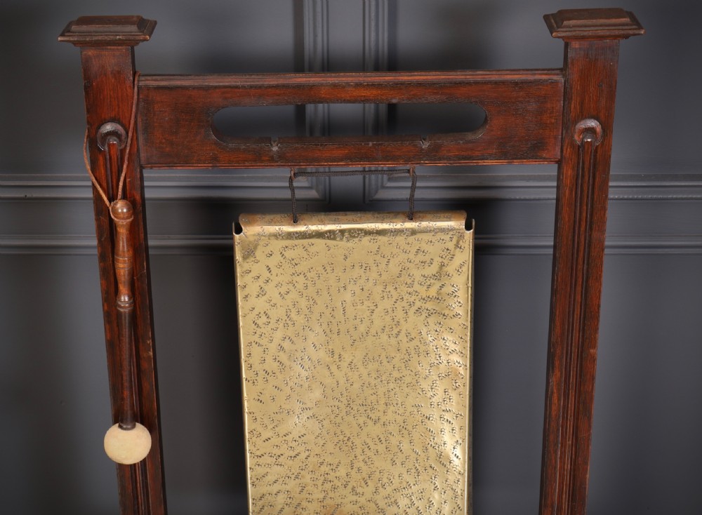 A freestanding dark oak frame housing a suspended rectangular hammered brass dinner gong complete with a wooden striker. View IV