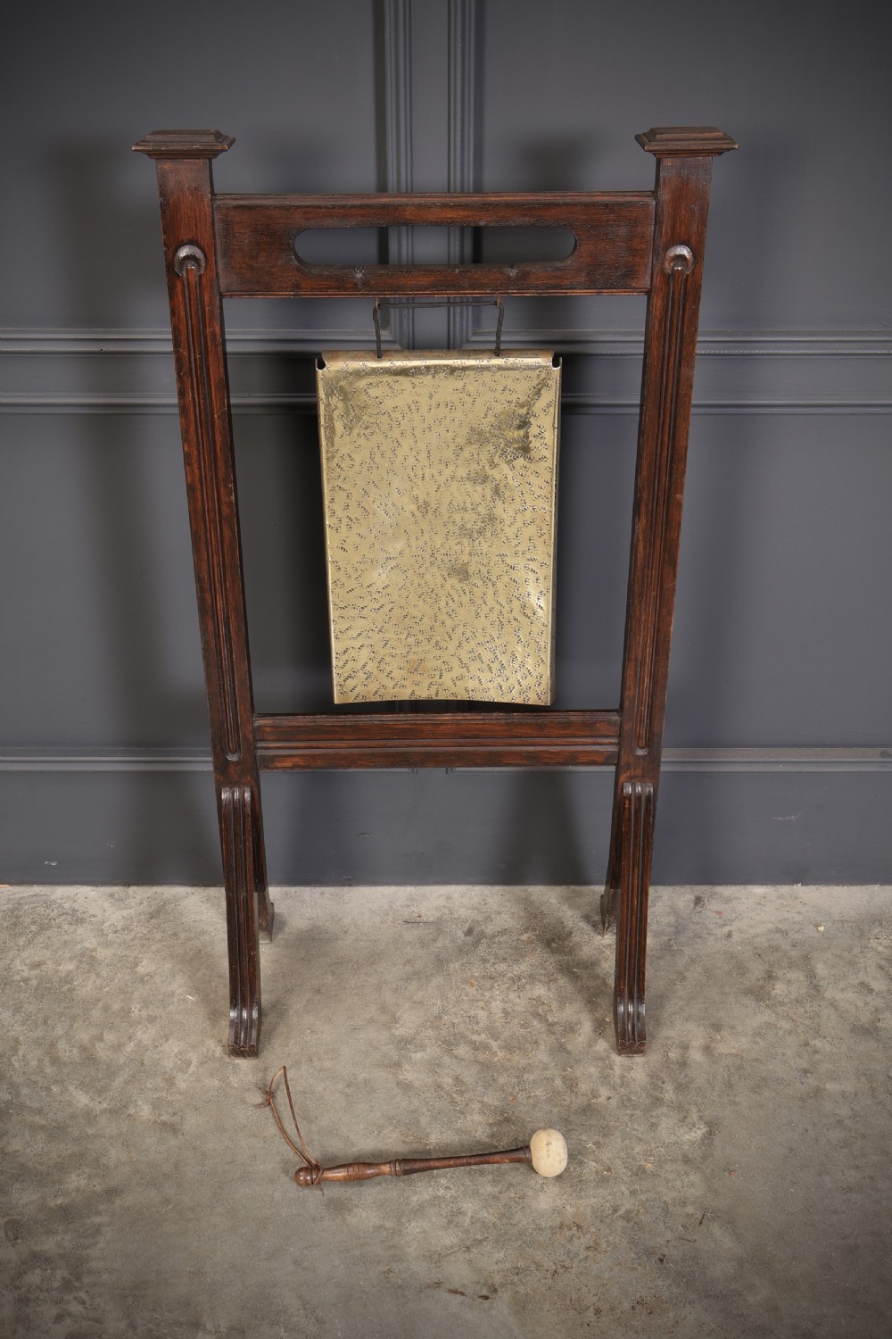 A freestanding dark oak frame housing a suspended rectangular hammered brass dinner gong complete with a wooden striker. View V