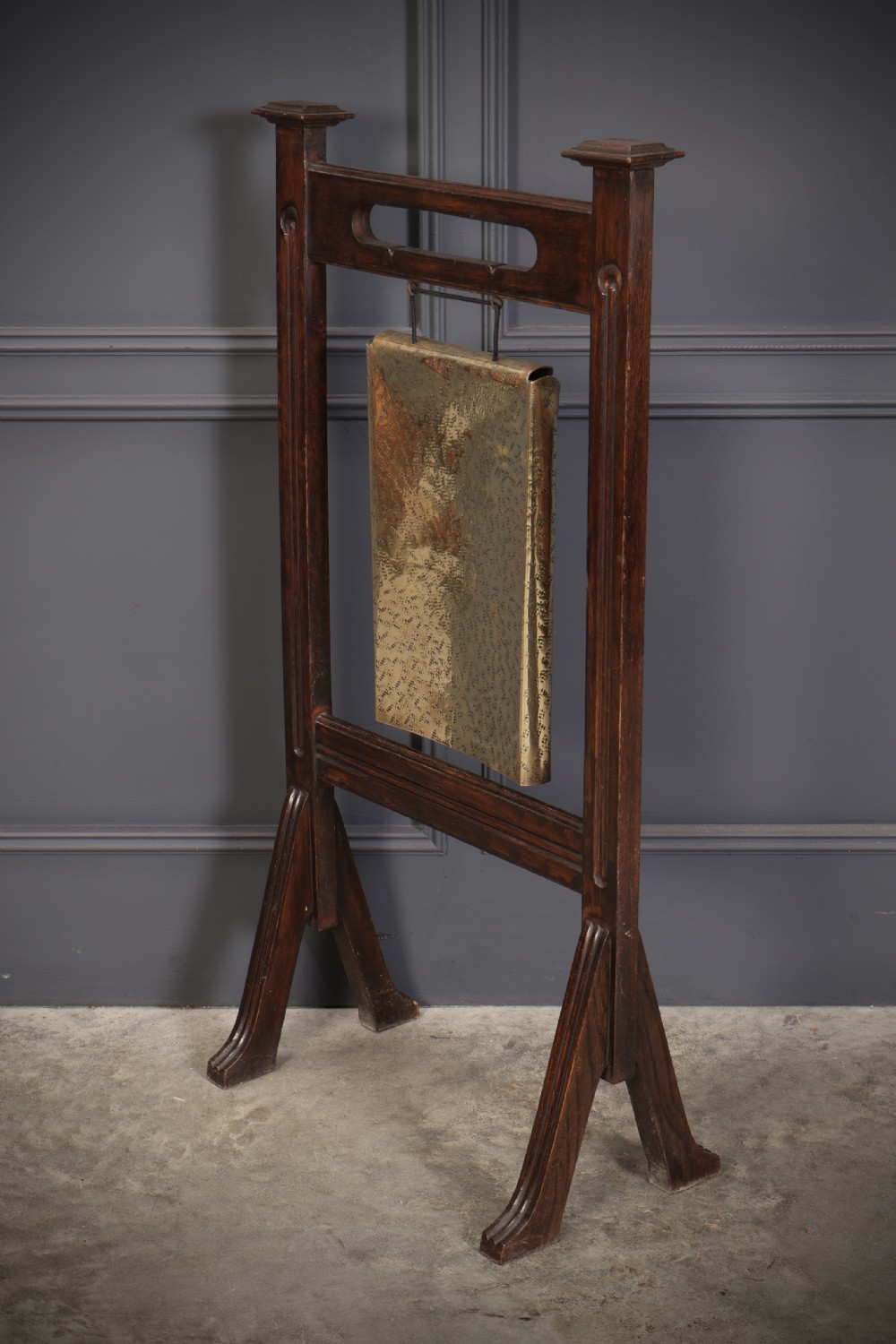 A freestanding dark oak frame housing a suspended rectangular hammered brass dinner gong complete with a wooden striker. View VI
