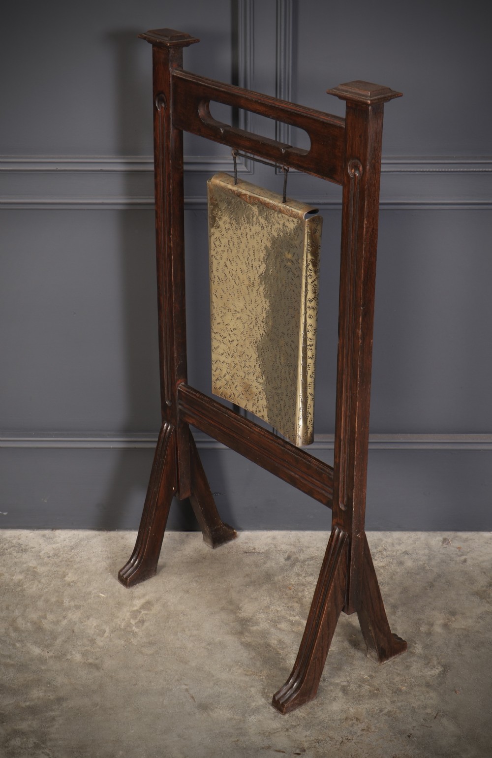 A freestanding dark oak frame housing a suspended rectangular hammered brass dinner gong complete with a wooden striker. View VII