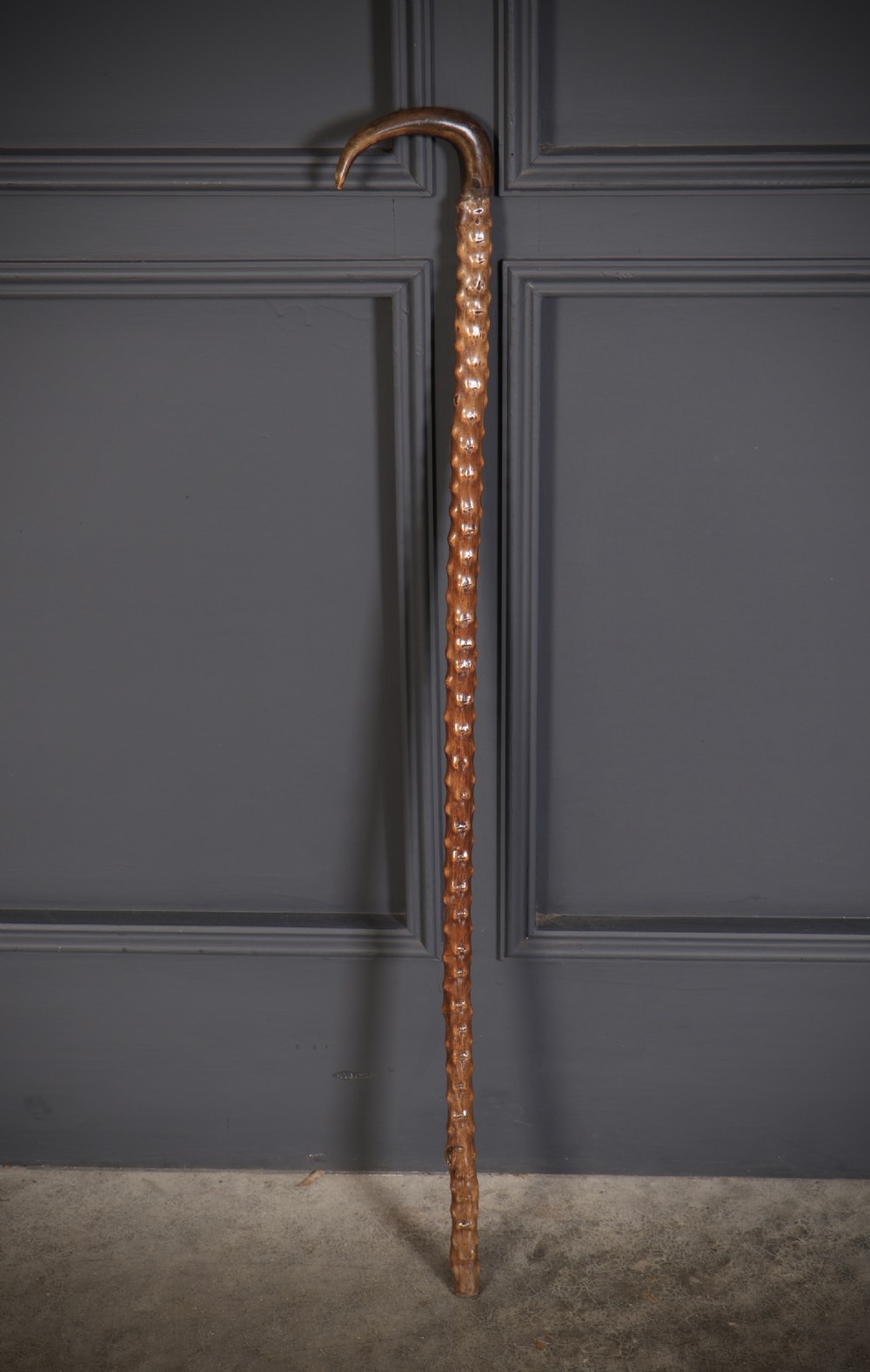 A wooden walking stick featuring a smooth curved crook handle and a textured shaft with natural wood knots.