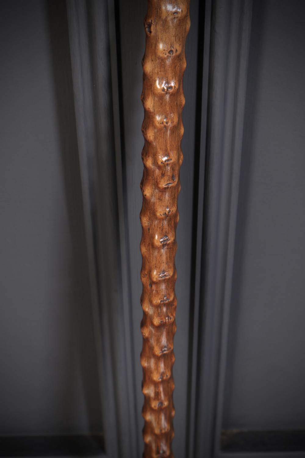 A wooden walking stick featuring a smooth curved crook handle and a textured shaft with natural wood knots. View III